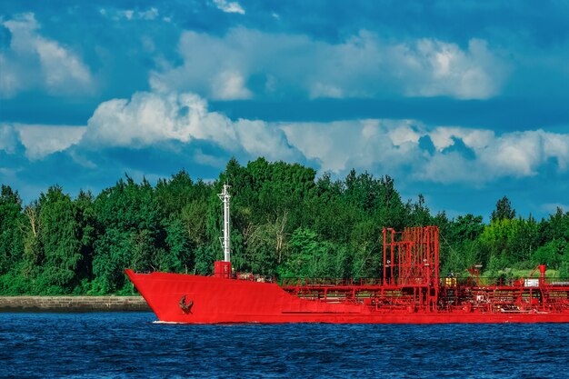 Navio-tanque de carga vermelho movendo-se à beira do rio