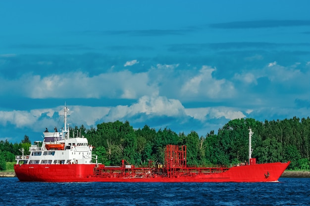 Navio-tanque de carga vermelho movendo-se à beira do rio