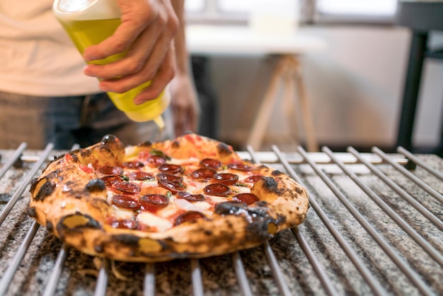 Neapolitanischer Pizza-Stil Nahaufnahme Küchenchef würzt Olivenöl über Chorizo-Wurst-Pizza auf dem Pizza-Kühlregal auf der Küchentheke, bevor er italienische frisch gebackene Napoli-Pizza serviert