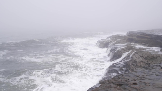 Nebelige Meereslandschaftswellen, die bei stürmischem Nebelwetter am Meeresstrand abstürzen