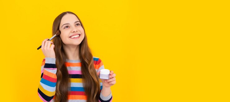 Foto se necesita maquillaje para parecer natural. niña feliz se maquilla. niño sonríe usando pincel de fundación. cosméticos para adolescentes. diseño de carteles para niños.