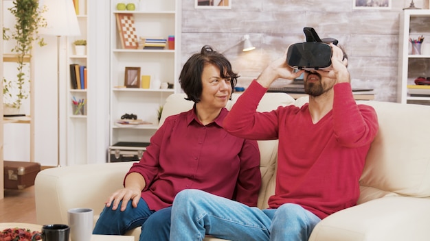 Neffe zeigt seiner Großmutter, wie man eine VR-Brille im Wohnzimmer benutzt.