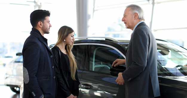 Negociante de carro, mostrando um carro para um casal