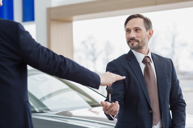 Negociante de carro profissional, passando as chaves para o seu novo proprietário de carro