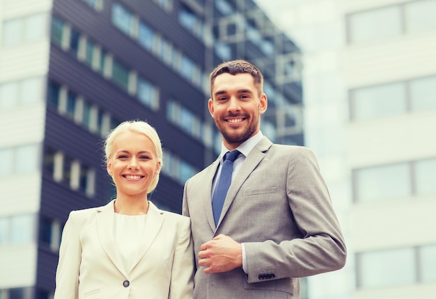 negocio, asociación, éxito y concepto de personas - hombre de negocios sonriente y mujer de negocios de pie sobre el edificio de oficinas