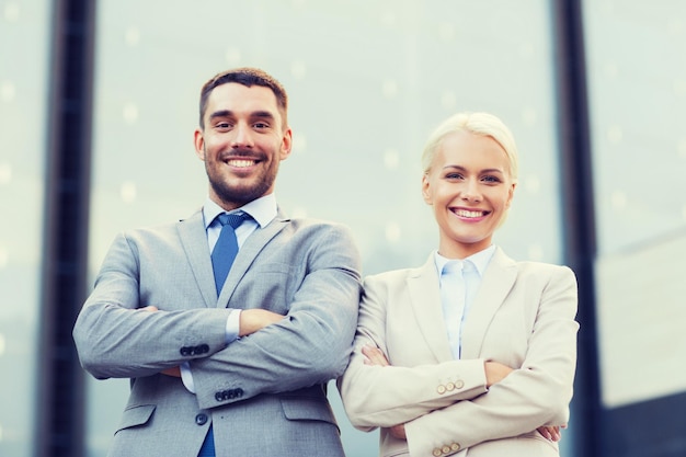 negocio, asociación, éxito y concepto de personas - hombre de negocios sonriente y mujer de negocios de pie sobre el edificio de oficinas