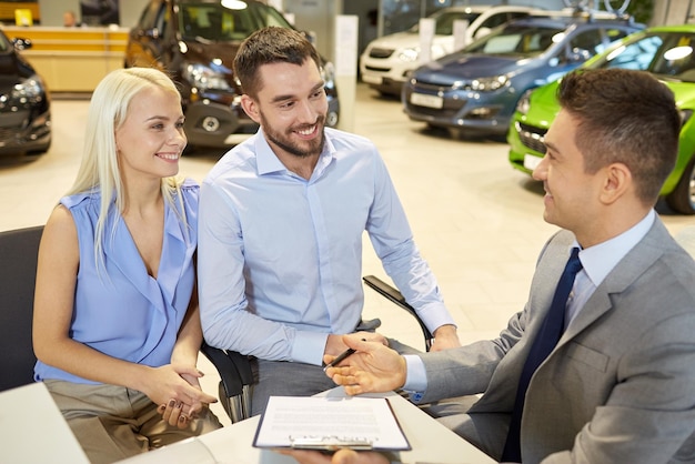 negócio automotivo, venda e conceito de pessoas - casal feliz com revendedor comprando carro no salão ou salão de automóveis