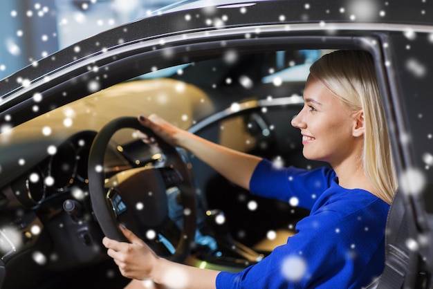 negocio de automóviles, venta de automóviles, consumismo, transporte y concepto de personas: mujer feliz sentada o conduciendo un automóvil sobre el efecto de la nieve