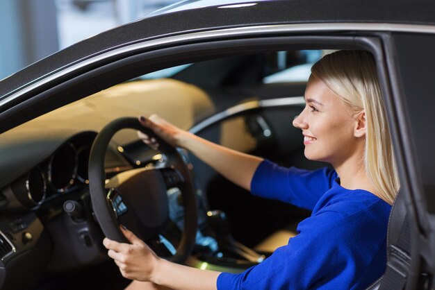 negocio de automóviles, venta de automóviles, consumismo, transporte y concepto de personas - mujer feliz sentada o conduciendo un automóvil