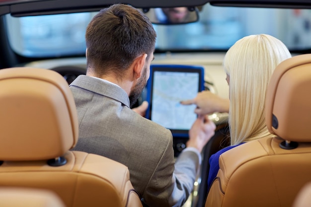 Foto negocio de automóviles, venta de automóviles, navegación y concepto de personas: cierre de una pareja sentada en un automóvil descapotable con computadora de tablet pc en el salón de automóviles o en el salón desde atrás