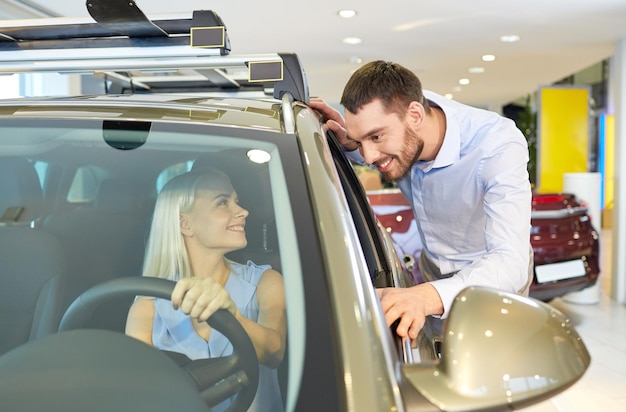 negocio de autos, venta de autos, consumismo y concepto de personas - pareja feliz comprando autos en auto show o salón