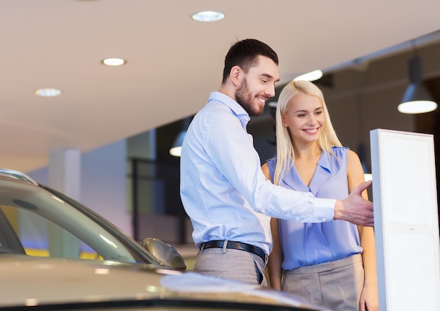 negocio de autos, venta de autos, consumismo y concepto de personas - pareja feliz comprando autos en auto show o salón