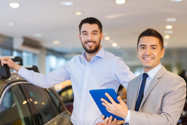 negocio de autos, venta de autos, tecnología y concepto de personas - hombre feliz y concesionario de autos con computadora de tablet pc en auto show o salón