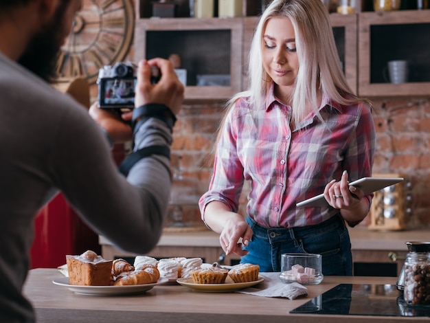 Negocio de blogs de comida. Estilo de vida de pareja. Hombre mujer de tiro apuntando a muffin. Surtido de pasteles alrededor.