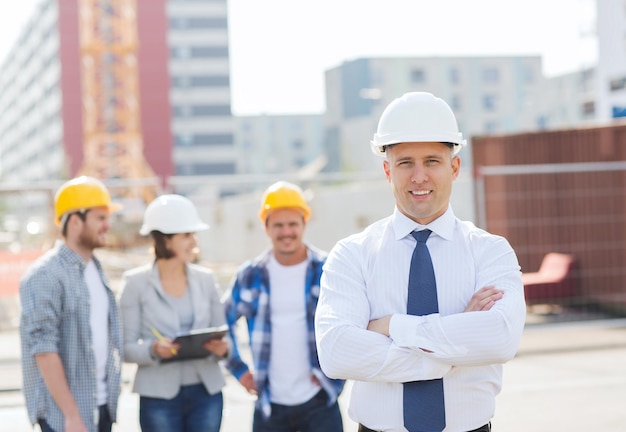 negocio, construcción, trabajo en equipo y concepto de personas - grupo de constructores sonrientes en cascos al aire libre