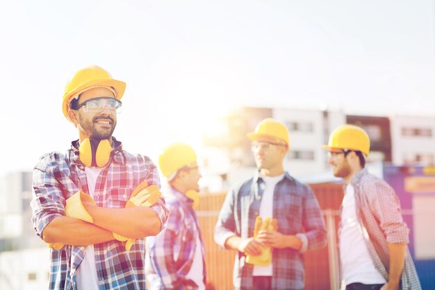 Foto negocio, construcción, trabajo en equipo y concepto de personas - grupo de constructores sonrientes en cascos con portapapeles al aire libre