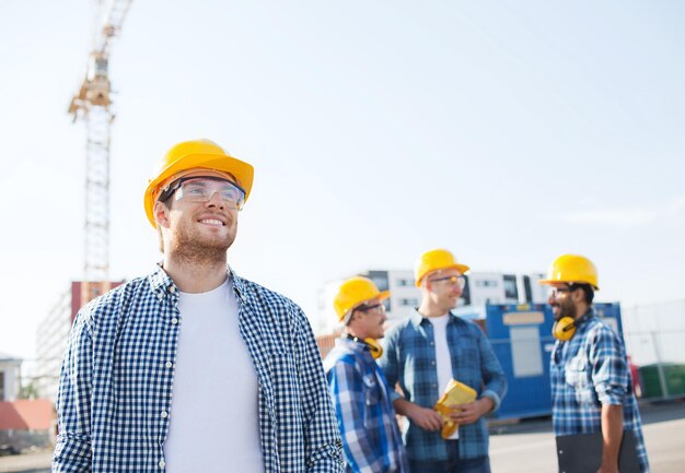 negocio, construcción, trabajo en equipo y concepto de personas - grupo de constructores sonrientes en cascos con portapapeles al aire libre