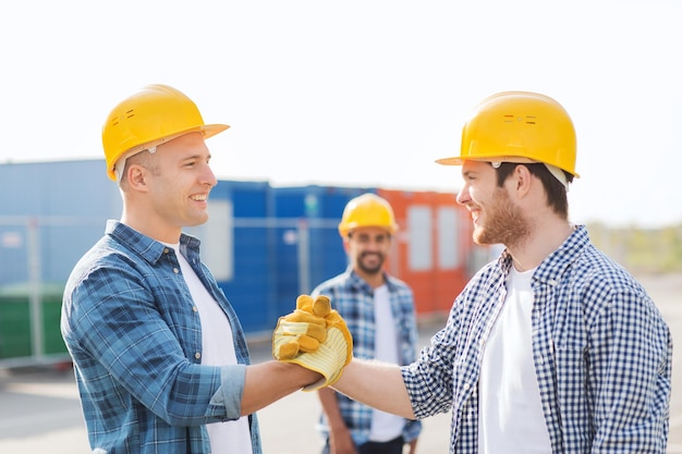 negocio, construcción, trabajo en equipo, gesto y concepto de personas - grupo de constructores sonrientes en cascos saludándose unos a otros con apretón de manos al aire libre