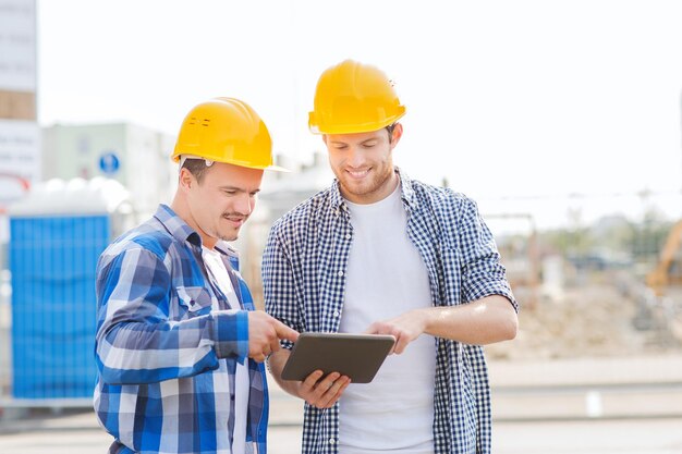 negocio, construcción, trabajo en equipo, tecnología y concepto de personas - grupo de constructores sonrientes en cascos con computadora de tablet pc al aire libre