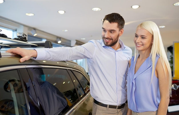 negócio de automóveis, venda de carros, consumismo e conceito de pessoas - casal feliz comprando carro no salão ou salão de automóveis