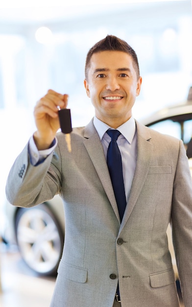 negócio de automóveis, venda de carros, consumismo e conceito de pessoas - homem feliz mostrando a chave no salão de automóveis ou salão