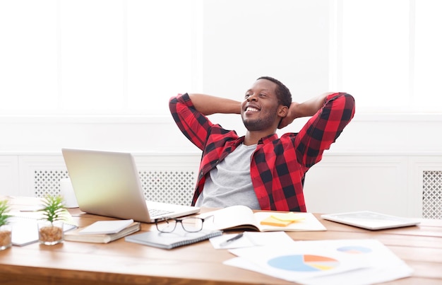 Negócio de sucesso em copos. Empresário negro relaxado casual com laptop no interior de um escritório branco moderno, copie o espaço