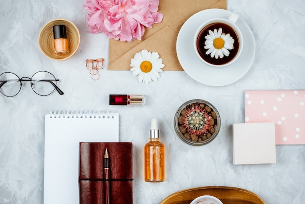 Negocio femenino con artículos de papelería, margaritas, flores de peonía, cuadernos y vasos, capa plana en la pared de cemento