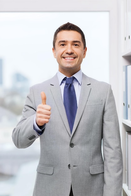 negocio, gente, gesto y concepto de éxito - hombre de negocios sonriente feliz en traje mostrando los pulgares para arriba en la oficina