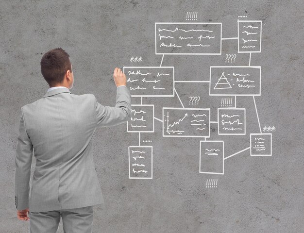 negocio, gente, publicidad, información y concepto de oficina - hombre de negocios escribiendo o dibujando un esquema sobre un fondo de pared de hormigón desde atrás