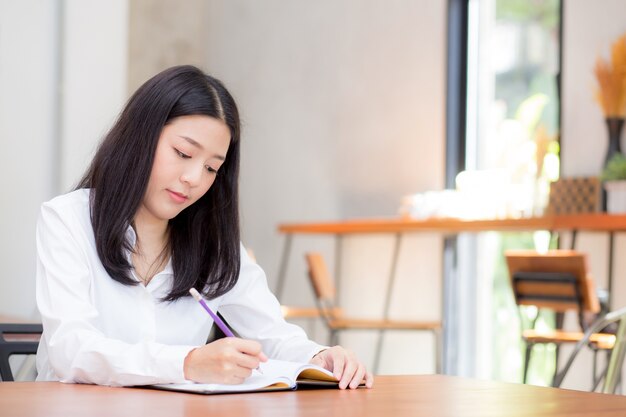 Negocio hermoso asiático joven escribiendo en el cuaderno en la mesa.