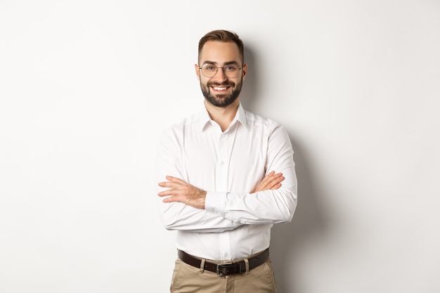 Negocio. joven empresario profesional en gafas sonriendo a la cámara, cruzando el brazo sobre el pecho con confianza, de pie sobre fondo blanco.