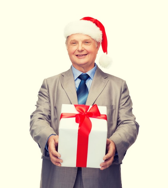 negocio, navidad, navidad, concepto de la felicidad - anciano sonriente en traje y sombrero del ayudante de santa con el regalo