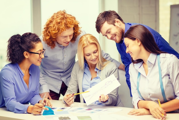 negocio, oficina, diseño de ropa y concepto de puesta en marcha - equipo creativo sonriente mirando boceto