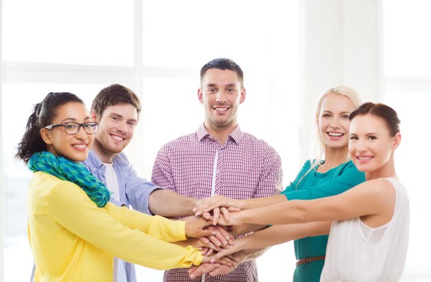 Foto negocio, oficina, gesto y concepto de puesta en marcha - equipo creativo sonriente con las manos una encima de la otra sentado en la oficina