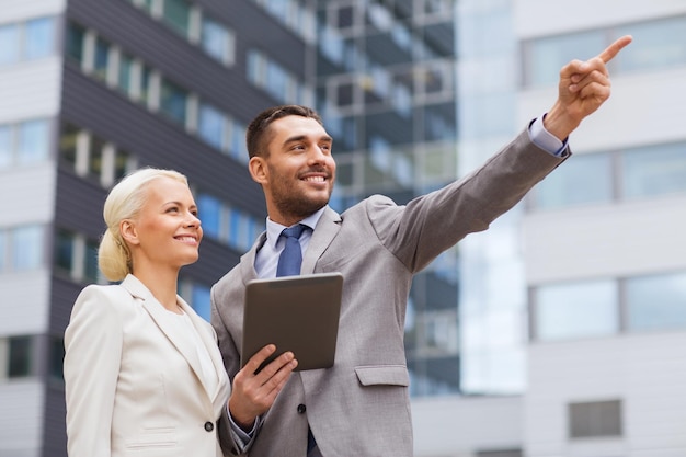 negocio, sociedad, tecnología y concepto de personas - hombre de negocios sonriente y mujer de negocios con computadora de tablet pc sobre el edificio de oficinas