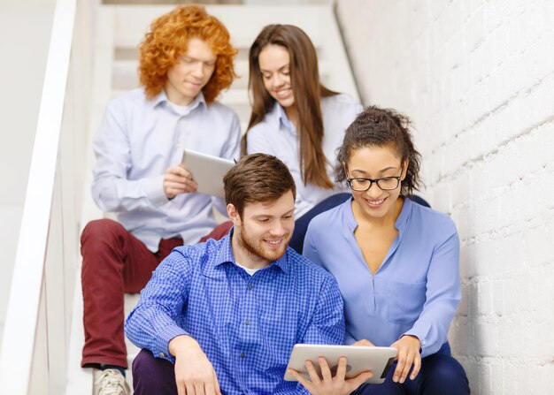 negocio, tecnología y concepto de puesta en marcha - equipo creativo sonriente con tablet pc sentado en la escalera