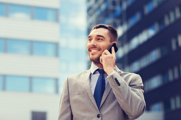 Foto negócio, tecnologia e conceito dos povos - homem de negócios de sorriso com smartphone que fala sobre o prédio de escritórios