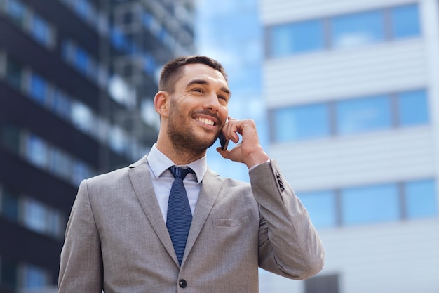 Negócio, tecnologia e conceito dos povos - homem de negócios de sorriso com smartphone que fala sobre o prédio de escritórios