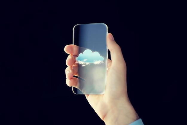 negocio, tecnología futura, computación y concepto de personas: cierre de la mano masculina sosteniendo y mostrando un teléfono inteligente transparente con nubes sobre fondo negro