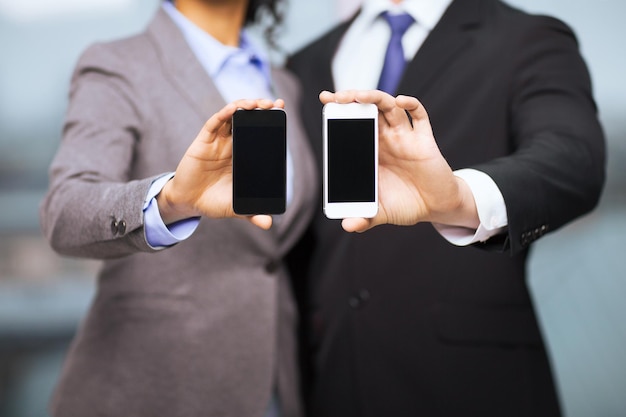 negocio, tecnología, internet y concepto de oficina - hombre de negocios y mujer de negocios con pantallas de smartphone negras en blanco en la oficina