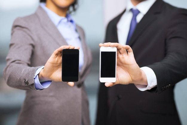 negocio, tecnología, internet y concepto de oficina - hombre de negocios y mujer de negocios con pantallas de smartphone negras en blanco en la oficina