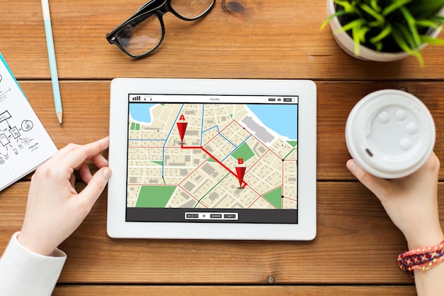 negocio, tecnología, personas y concepto de navegación: cierre de una mujer con un mapa del navegador GPS en la pantalla de la computadora de la tableta y café en una mesa de madera