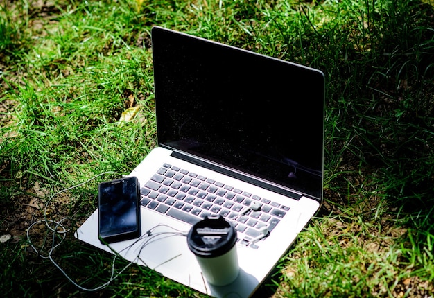 Negocios ágiles Lugar de trabajo de estudio en línea al aire libre Música gratis vibraciones de verano Cuaderno relajante con auriculares de teléfono móvil y café para ir a la vida de los estudiantes universitarios de hierba verde Compras en línea