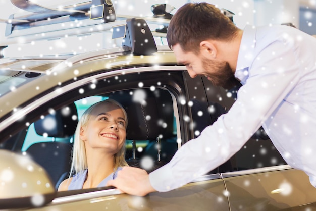 Foto negócios automotivos, venda de carros, consumismo e conceito de pessoas - casal feliz comprando carro em salão de automóveis ou salão sobre efeito de neve