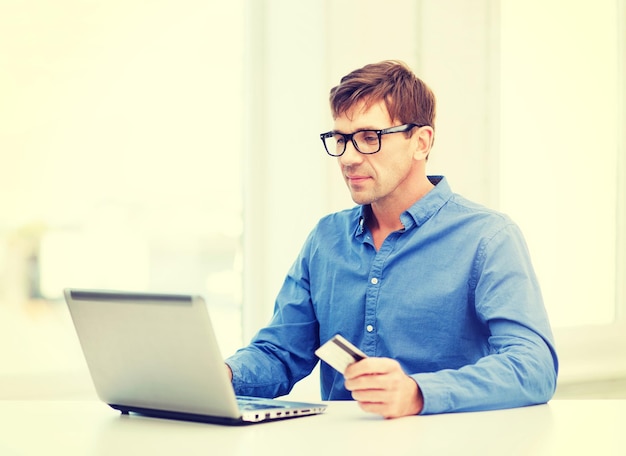 negócios, banco on-line, conceito de compras pela Internet - homem sorridente com laptop e cartão de crédito em casa