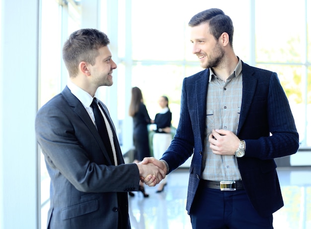 Negocios y concepto de oficina - dos hombres de negocios dándose la mano en la oficina