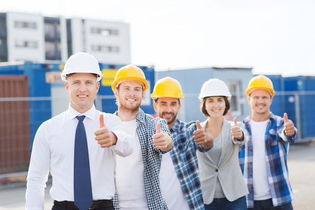 negócios, construção, trabalho em equipe, gesto e conceito de pessoas - grupo de construtores sorridentes em capacetes mostrando polegares para cima ao ar livre