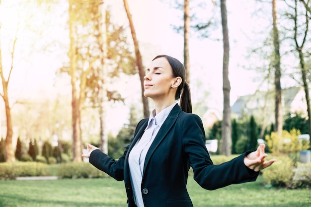 Negócios e meditação Uma linda mulher de negócios concentrada em um terno preto está sentada em uma posição de lótus na grama do parque da cidade e descansando depois do trabalho