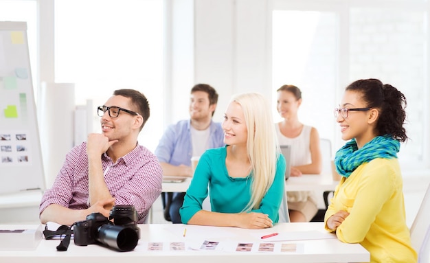 Foto negocios, educación, fotografía, oficina y concepto de puesta en marcha - equipo creativo sonriente con cámara fotográfica escuchando conferencias en la oficina