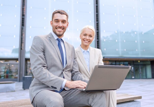 negocios, educación, tecnología y concepto de personas - empresarios sonrientes que trabajan con computadoras portátiles en las calles de la ciudad